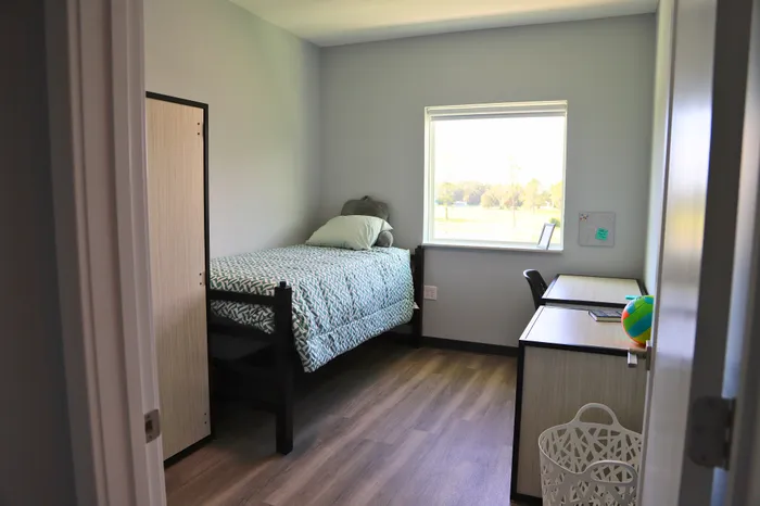 Bright and cozy bedroom with a single bed, wooden floor, and a sunny window view, perfect for a peaceful retreat.