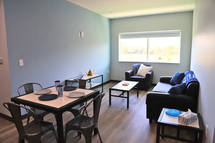 Bright and inviting living space with modern furniture, featuring a cozy sofa, elegant dining area, and large window offering scenic views.