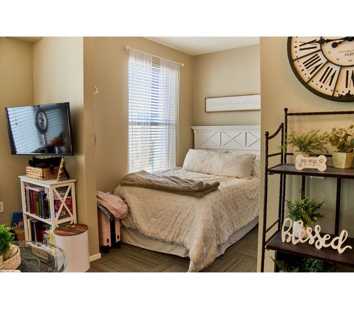 Cozy bedroom with plush bed, charming wall decor, and abundant natural light, perfect for relaxation and serenity.