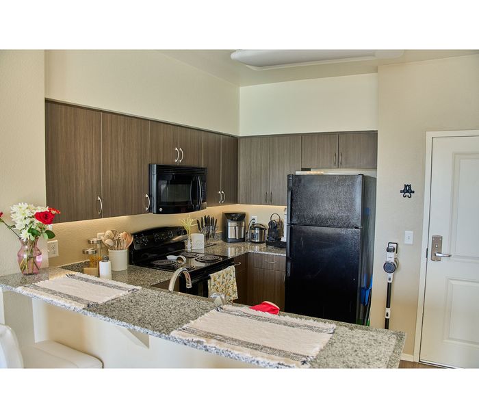 Modern kitchen with granite countertops, elegant dark wood cabinets, and sleek black appliances complemented by vibrant floral decor.