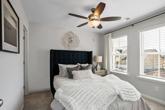 furnished bedroom model with windows and ceiling fan