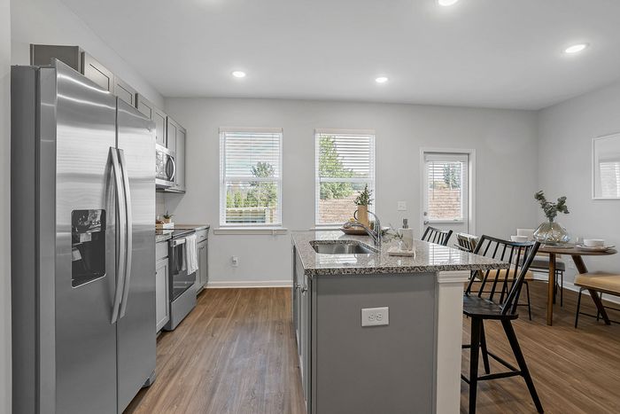 Pet-Friendly Townhomes in Acworth, GA -Covey HomesHunter Trail - Kitchen with Granite-Style Countertops, Grey Cabinets, Center Island, Windows, Stainless Steel Appliances, and Door Leading to Backyard.