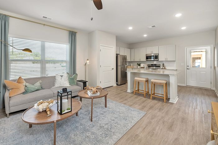 Furnished living room with rug, couch, and one window with view of kitchen with stainless steel appliances