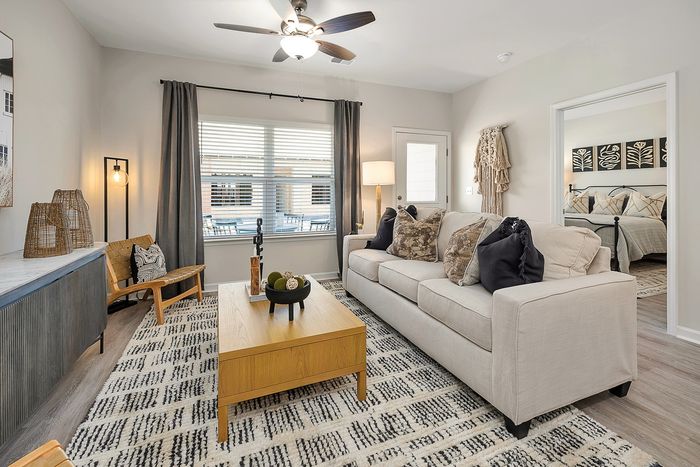 Three-BR Homes in Brunswick, GA - Covey Homes Fox Run - Furnished Living Room with Sofa, Ceiling Fan, Wood-Style Flooring, and a Wide Window.