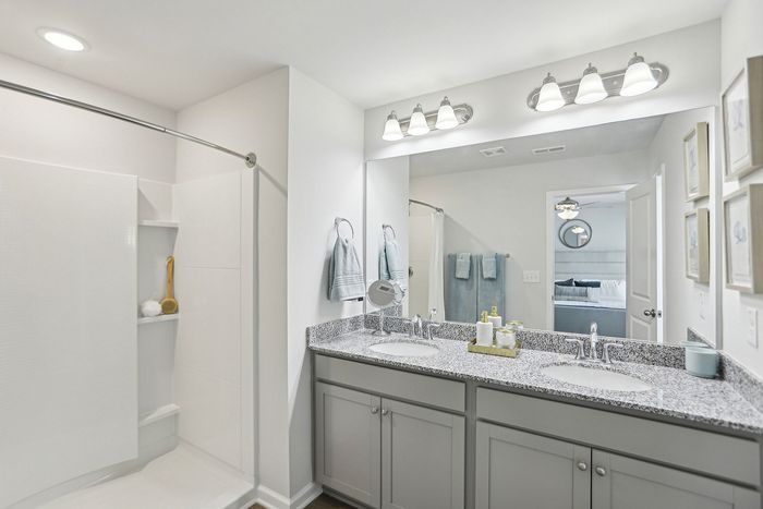 bathroom with two sinks, mirror, lighting fixtures, light gray cabinets, and shower stall