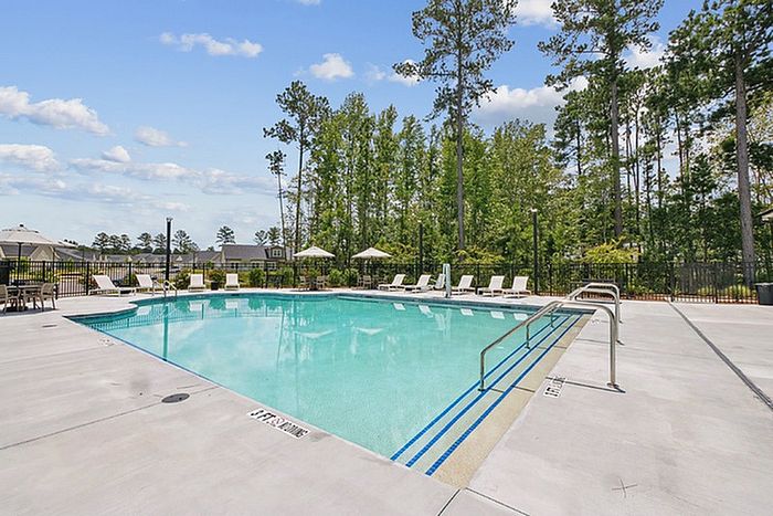 Inviting outdoor swimming pool surrounded by lush greenery, featuring sun loungers and umbrellas under a clear blue sky.
