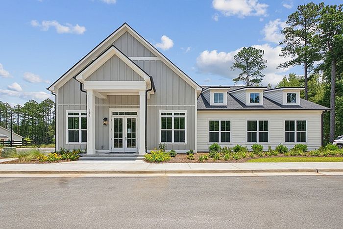 Charming modern home with a grand entrance, large windows, and beautiful landscaping under a clear blue sky.