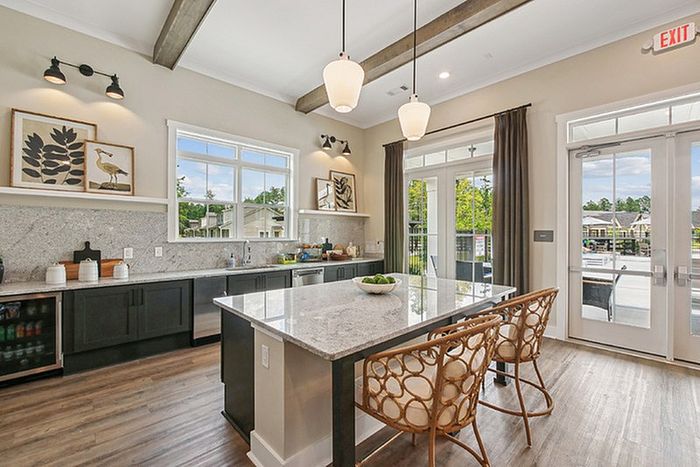 Chic modern kitchen with elegant island, pendant lighting, and natural views through large windows.