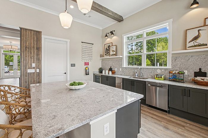Modern kitchen featuring sleek granite countertops, elegant pendant lighting, and large windows with a view of greenery.