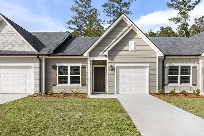 Charming modern townhouse with a sleek gray exterior, double garage doors, and lush green lawn, ideally situated in a serene neighborhood.