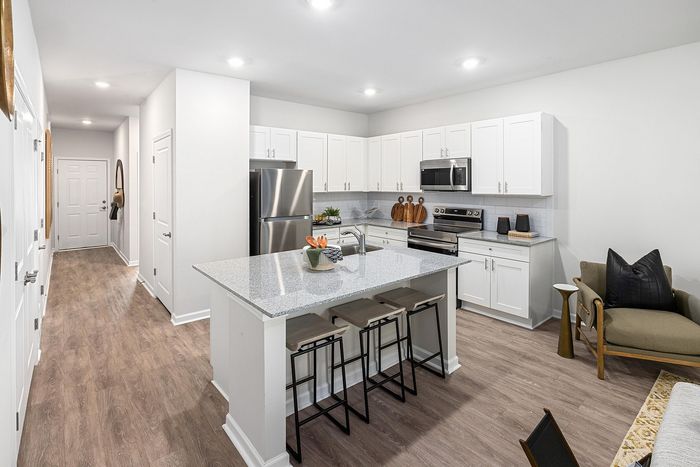 Modern kitchen with sleek white cabinetry, granite countertops, and stainless steel appliances, adjacent to a cozy living area with stylish seating.