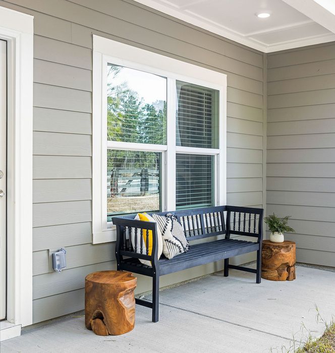 Charming front porch with a stylish black bench, accent pillows, natural wood stools, and serene views through the window.