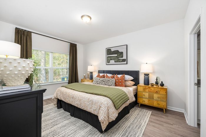 Bright and elegant bedroom featuring a cozy bed with decorative pillows, chic bedside lamps, and a natural view outside the large window.