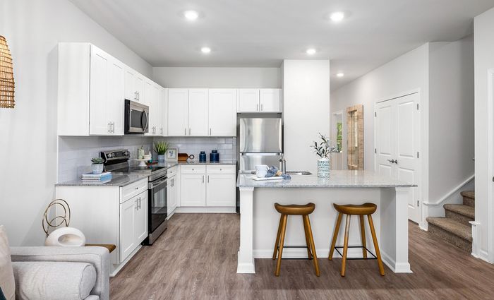 Bright, modern kitchen with sleek white cabinetry, stainless steel appliances, and elegant bar seating on wooden flooring.