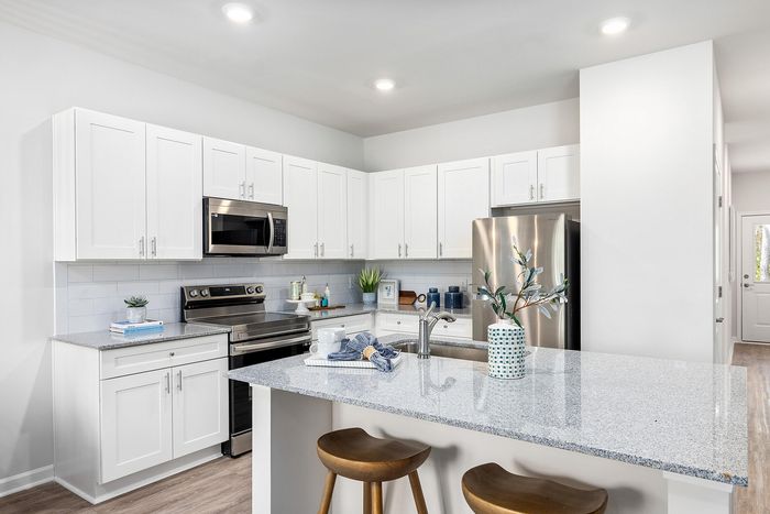 Chic modern kitchen featuring sleek white cabinetry, stainless steel appliances, light granite countertops, and stylish bar seating for two.