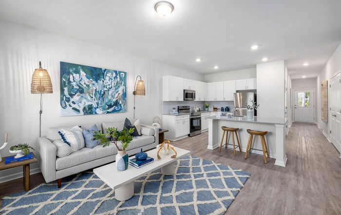 Modern open-concept living room with chic decor, featuring a cozy sofa, stylish artwork, and a sleek kitchen with a breakfast bar and stools.