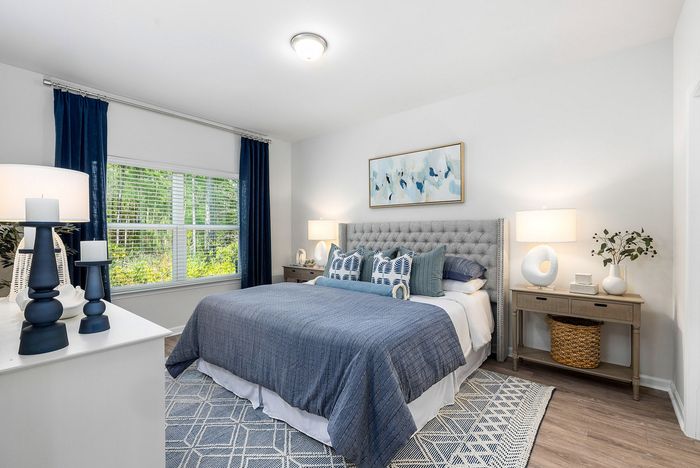 Bright and cozy bedroom with elegant decor, featuring a plush bed with blue accents, modern side tables, and a large window with calming views.