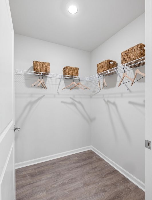 Spacious walk-in closet featuring elegant wood flooring, organized wire shelving, and stylish wicker baskets.