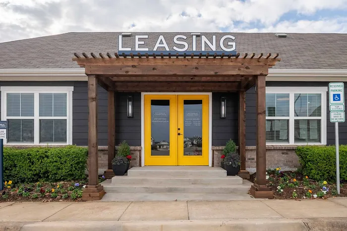 Charming leasing office entrance with vibrant yellow doors, welcoming porch, and lush landscaping.