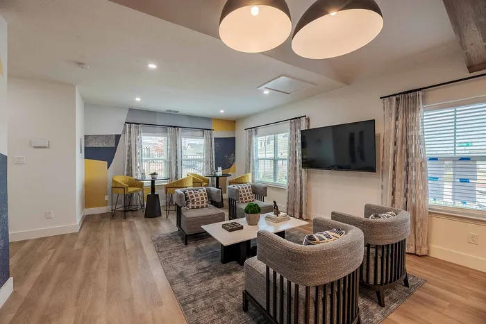 Modern and inviting living room with stylish gray chairs, bright yellow accent chairs, large windows, and a sleek flat-screen TV. Warm natural light enhances the cozy ambiance.