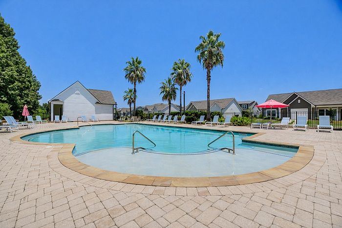 Inviting outdoor swimming pool surrounded by lounge chairs and swaying palm trees, offering a relaxing oasis under a clear blue sky.