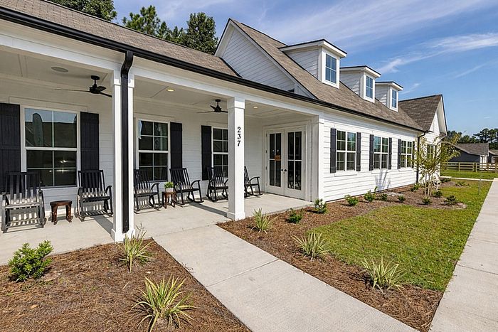Inviting modern ranch-style home with charming front porch, comfortable rocking chairs, and manicured landscaping under clear blue skies.