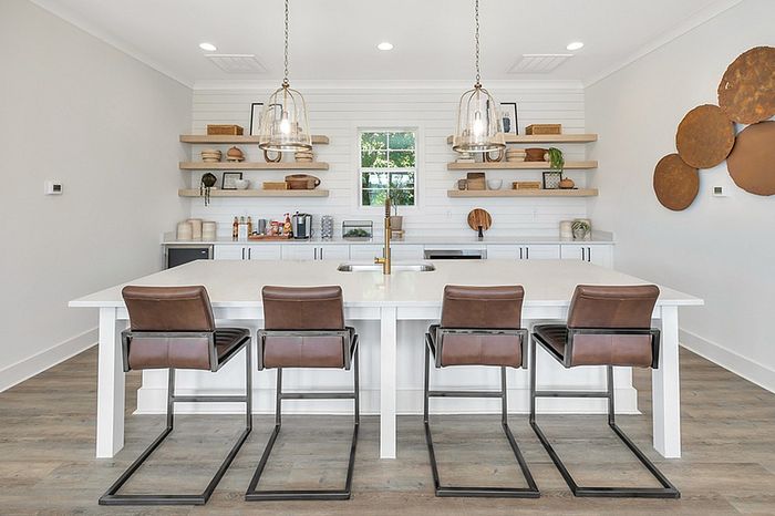 Modern kitchen with sleek white island, stylish pendant lights, open shelving, and elegant leather bar stools, creating a chic and inviting space.