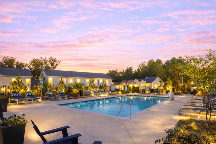 Luxurious resort-style pool area with elegant lounge chairs, ambient lighting, and lush greenery under a breathtaking sunset sky.