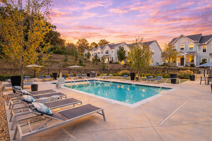 Charming residential complex with an inviting swimming pool, surrounded by lush greenery under a stunning sunset sky.