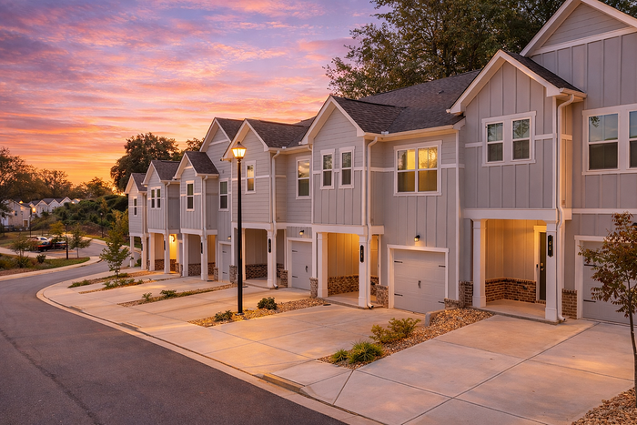 Charming row of modern townhouses with illuminated exteriors, nestled in a tranquil neighborhood under a stunning sunset sky.