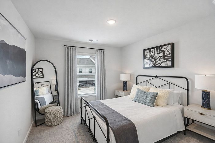 Elegant bedroom featuring a cozy bed with stylish metal frame, modern lamps, serene artwork, and a full-length mirror reflecting light from the large window.