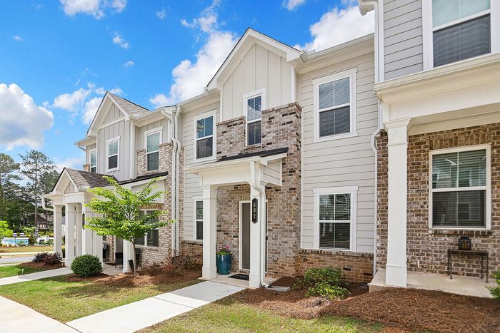 Charming townhouse exterior with modern brick and siding design, lush landscaping, and a welcoming front porch under a bright blue sky.