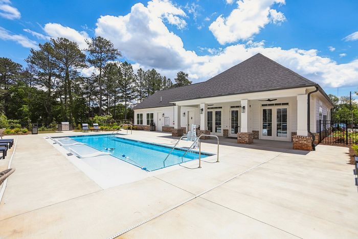 Charming outdoor pool area with modern seating, surrounded by lush greenery and a stylish clubhouse.