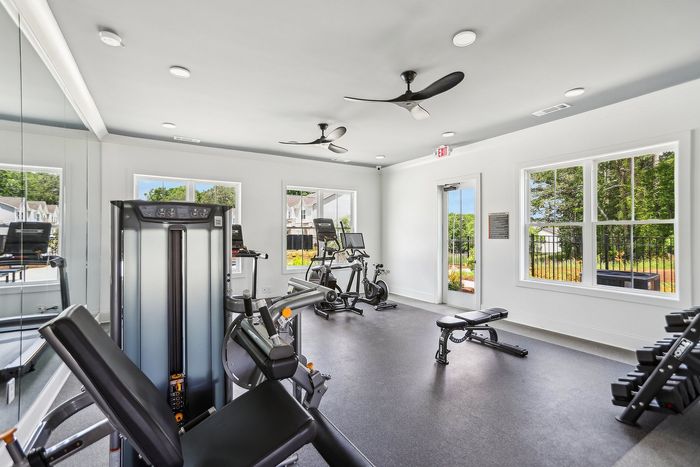 Bright and modern fitness center with state-of-the-art equipment, large windows offering lush outdoor views, and a sleek interior design for an invigorating workout experience.