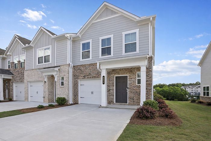 Charming two-story townhouse with a brick facade, modern garage, and inviting entryway, set against a picturesque suburban backdrop.