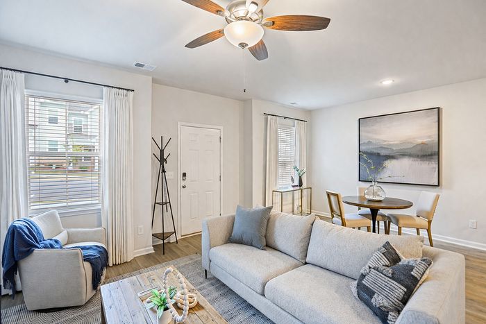 Inviting living room with a cozy beige sofa, modern ceiling fan, and a stylish dining area with wall art, offering a blend of comfort and elegance.