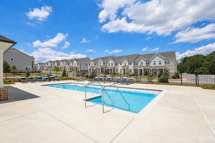 Inviting community pool with lounge chairs and beautiful townhouses in the background under a bright blue sky.