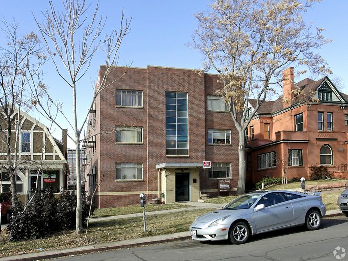 Charming brick apartment building nestled between two historic homes with parking in front.