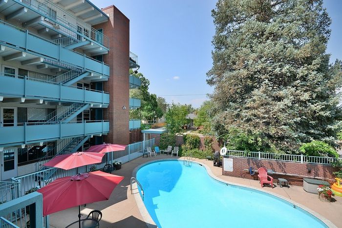 Inviting apartment complex with a pristine pool, red parasols, and lush greenery.