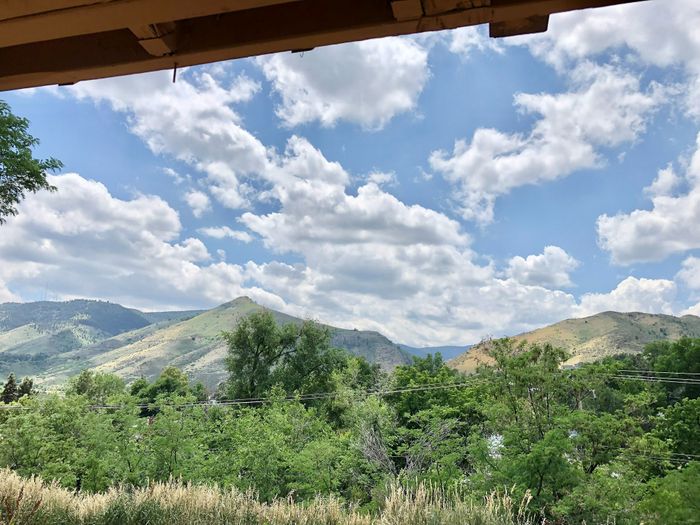 Stunning mountain landscape view from an apartment balcony, showcasing lush greenery and a vibrant blue sky with fluffy clouds.