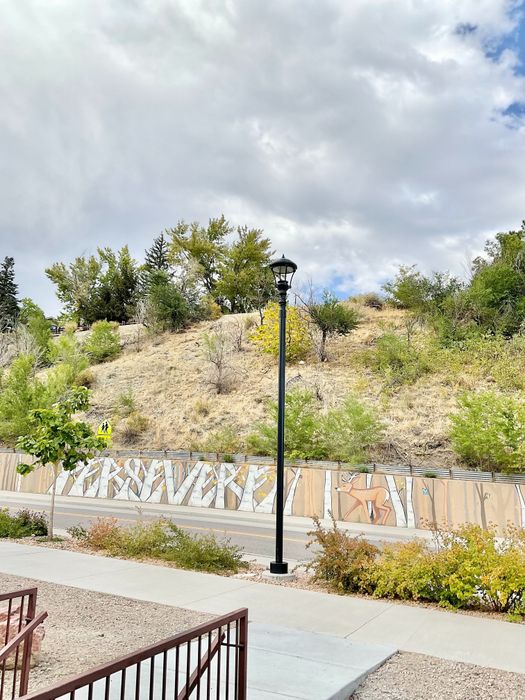 Charming hillside with artistic mural and lush greenery under a cloudy sky.