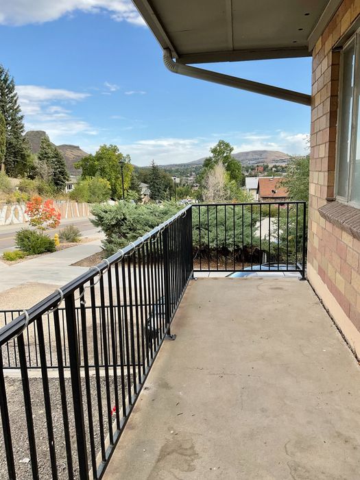 Charming balcony view overlooking lush greenery and distant hills, under a clear blue sky.