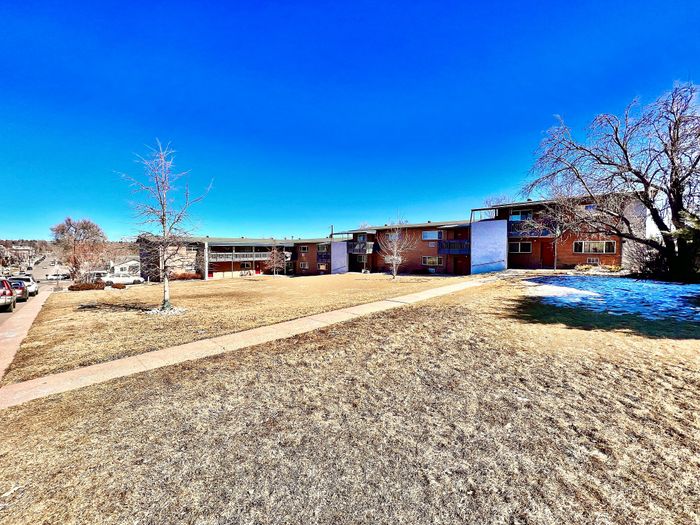 Charming suburban apartment complex surrounded by open green space and trees under a clear blue sky.