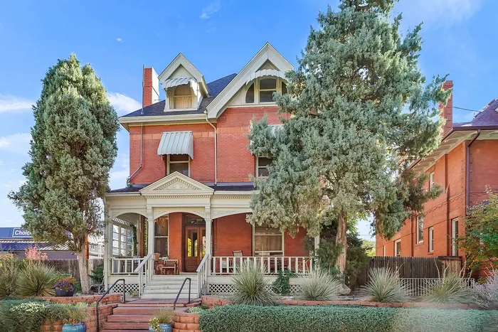 Elegant Victorian-style brick home with ornate porch and lush greenery.