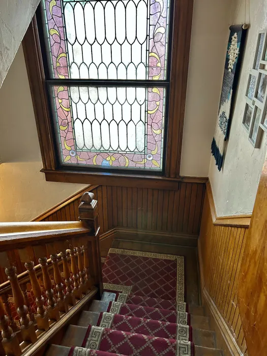 Elegant staircase featuring rich woodwork and intricate stained glass window with vibrant patterns.