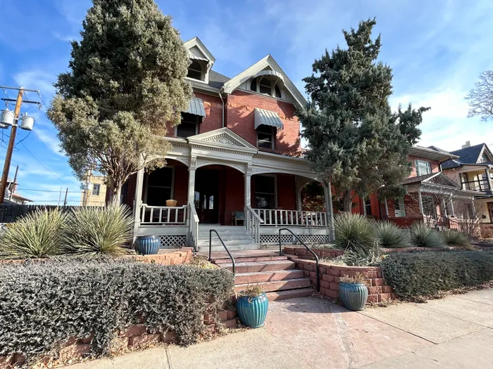Elegant Victorian-style brick home with a spacious porch, mature trees, and manicured landscaping.
