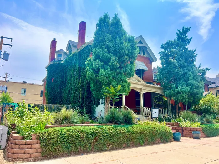 Elegant red brick house covered in lush greenery with a welcoming front porch and vibrant garden landscaping.