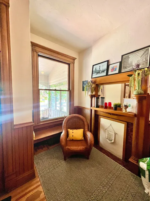 Inviting corner with a wicker chair, decorative fireplace, and natural light streaming through a tall window.