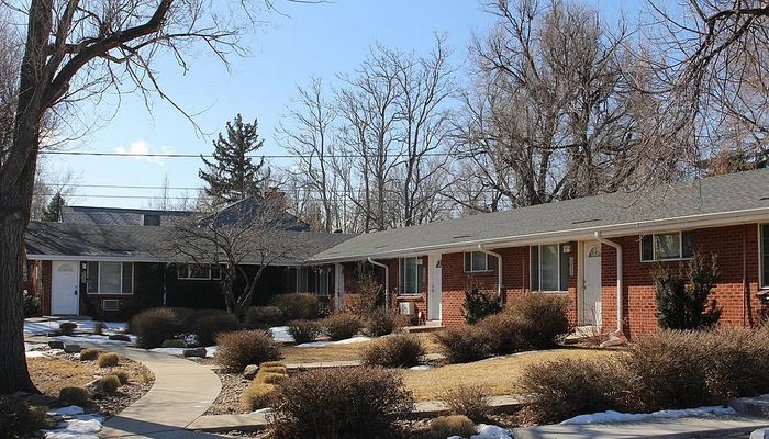 Quaint brick apartment complex surrounded by trees and a well-kept garden pathway.