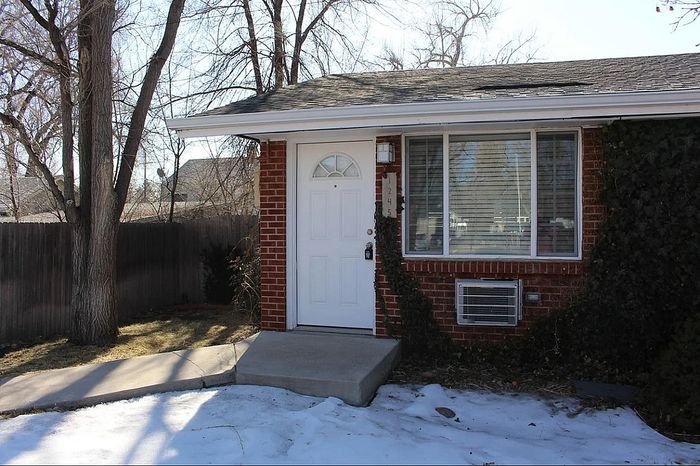 Cozy brick home with large front window, surrounded by trees and a wooden fence.